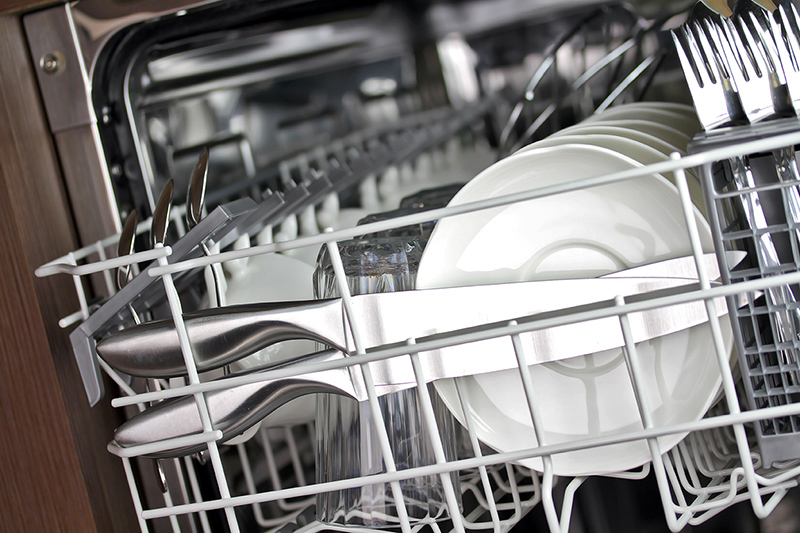 This loaded dishwasher has silverware, cups, and saucers.