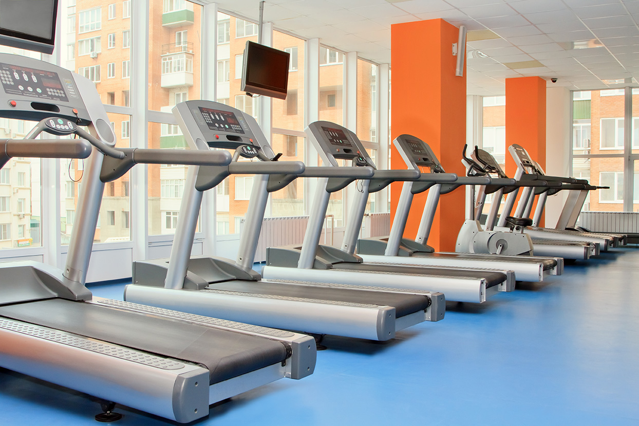 A fitness center with treadmills in a row on a blue floor.