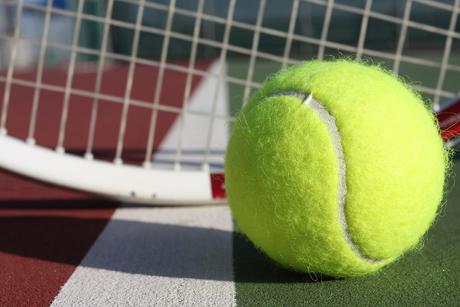 This tennis ball sits in front of a tennis racket on the court.