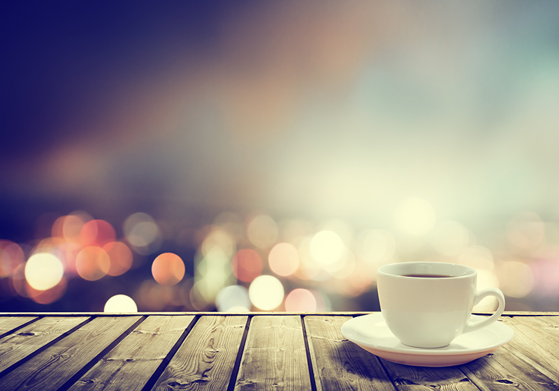 A cup of coffee with city lights in the background.
